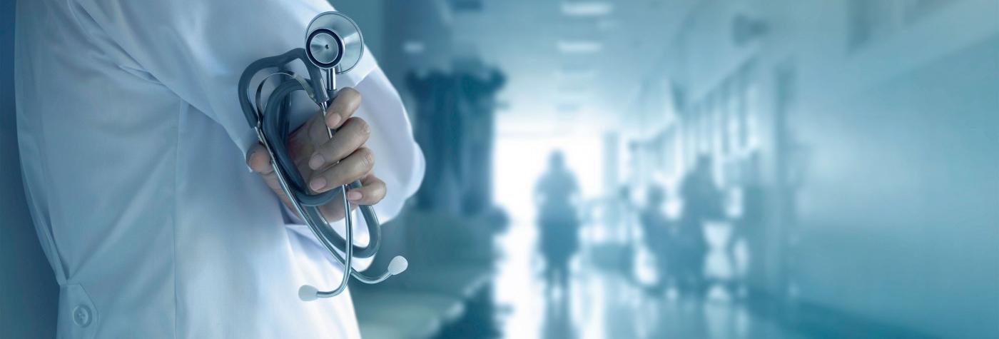 Image of medical provider holding a stethoscope with a hospital hallway in the background.