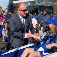 Coach Stoops shakes the hand of Audrey, a young white girl with blonde hair and a blue hat. She is sitting in the cart.