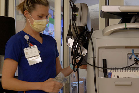 Nurse wearing blue scrubs and a mask uses equipment in the ICU.