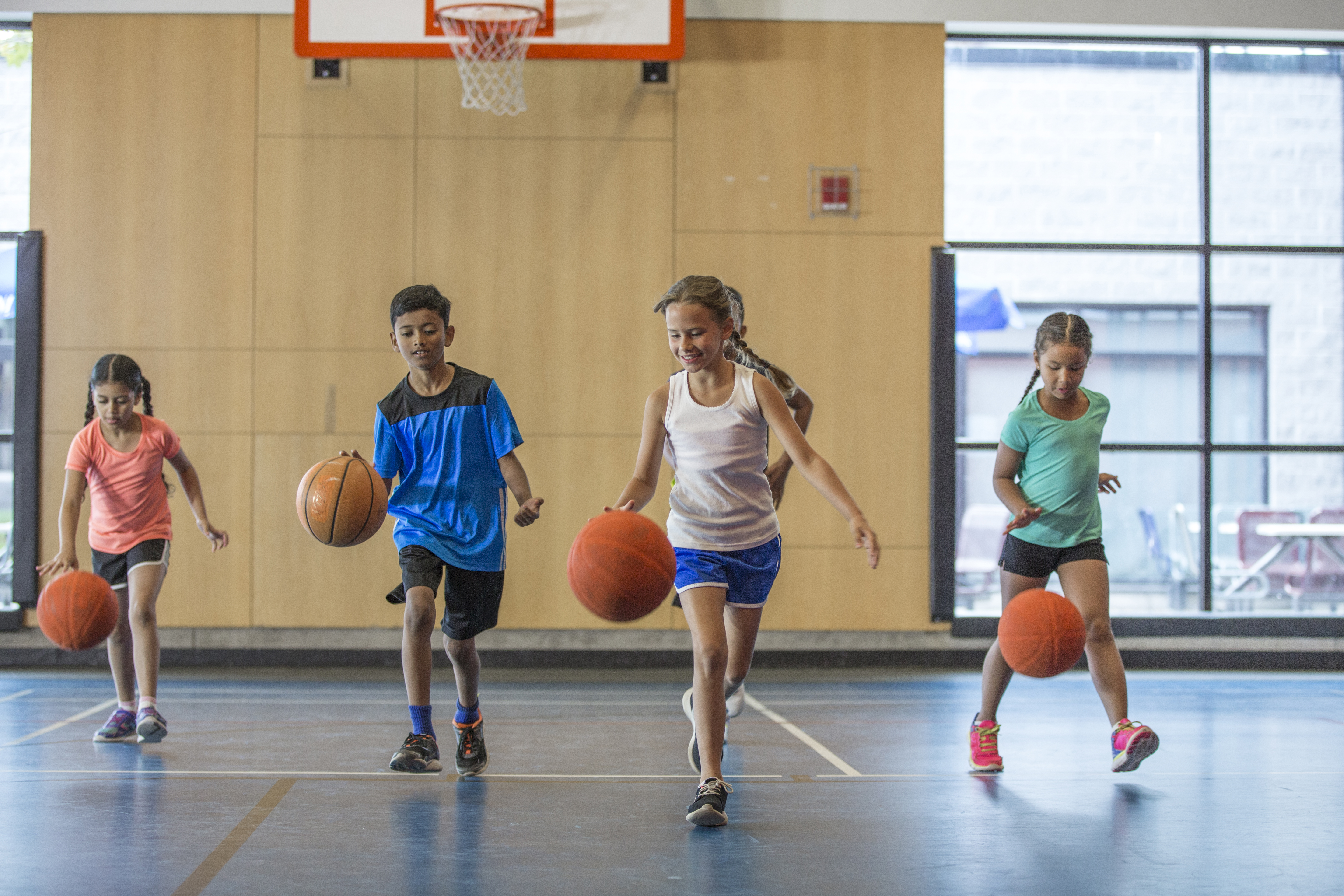 Four kids playing basketball in a gym.