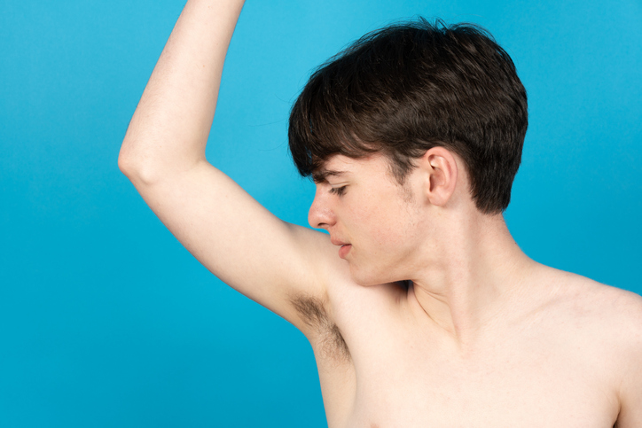 A teen boy smells his right armpit.