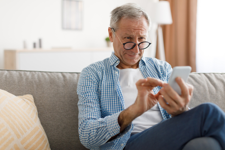 An older man with cataracts looks at his phone.