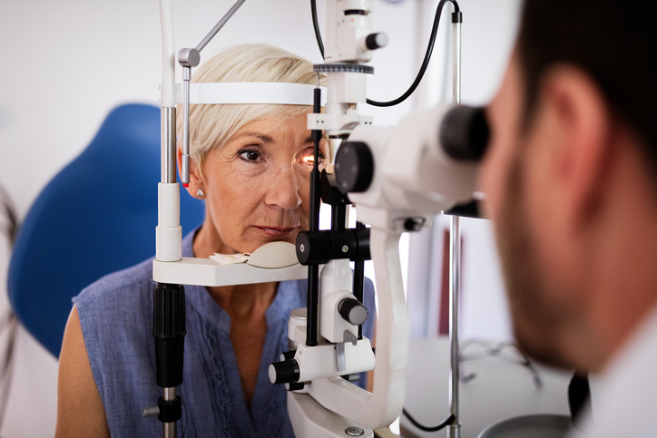 A woman in her 60's has her eyes examined by a doctor who is out of focus.