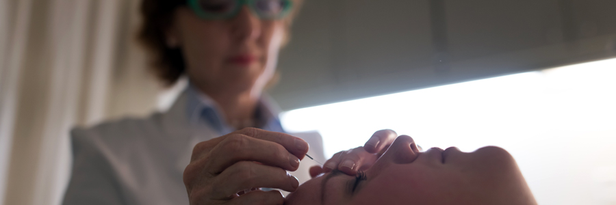 An acupuncturist inserts a needle into her patient's forehead.
