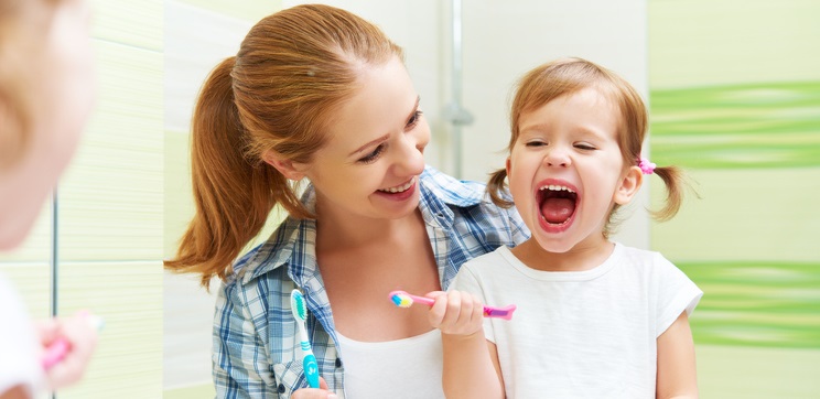 Mom teaches her daughter how to brush her teeth.