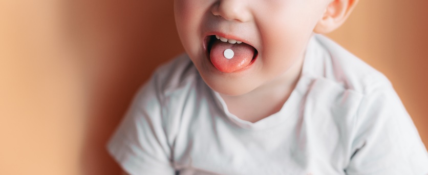 A child sticks his tongue out and has a pill in his mouth.