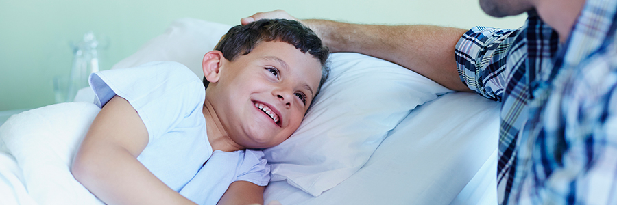 Happy boy holding father's hand while lying in bed at hospital bed