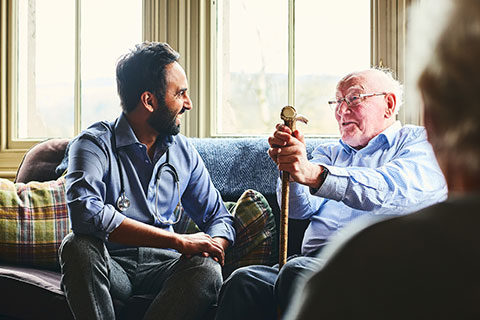 A community health worker visits an elderly male patient at home. 