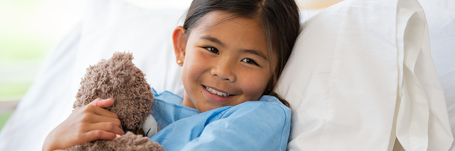 Girl hugging teddy bear in hospital bed