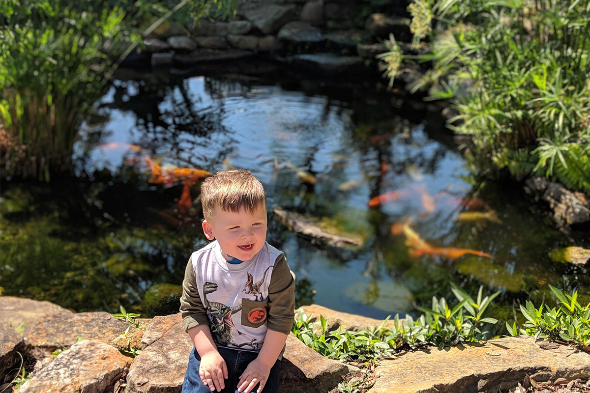 Kase Chaney sits beside a pond full of goldfish.