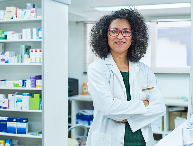 A pharmacist with her arms folded stands in the pharmacy.