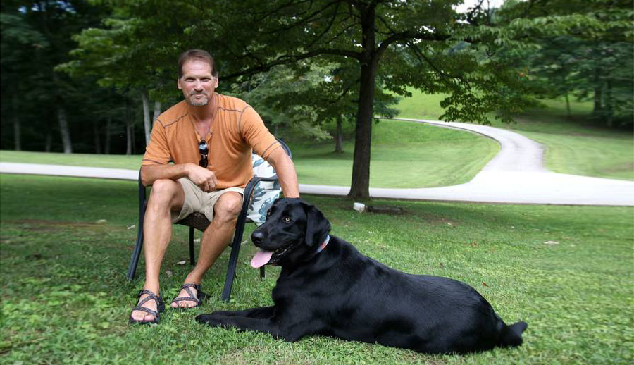 Myrl Sizemore sits outdoors with his dog, Sarge, at his feet.