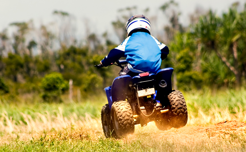 Child riding an all-terrain vehicle, wearing a helmet.