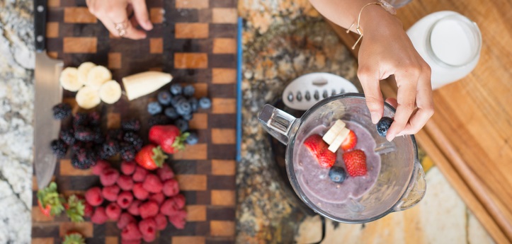 Woman places smoothie ingredients into blender.