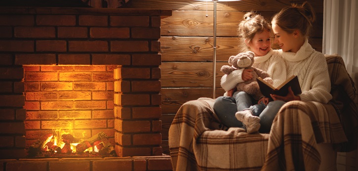 Mother and young daughter read by the fireplace.
