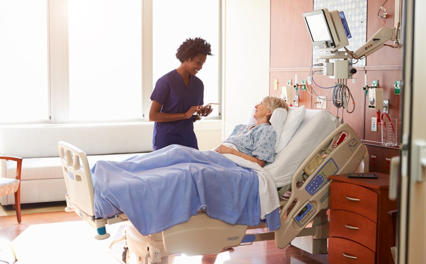 A female nurse talks with an elderly female patient in her hospital room.