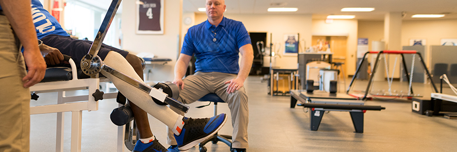 A sports rehabilitation patient lifts weights with physical therapists.