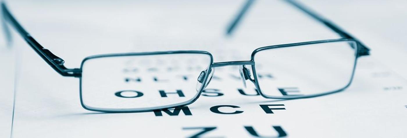 close-up of eyeglasses sitting on top of an eye testing chart