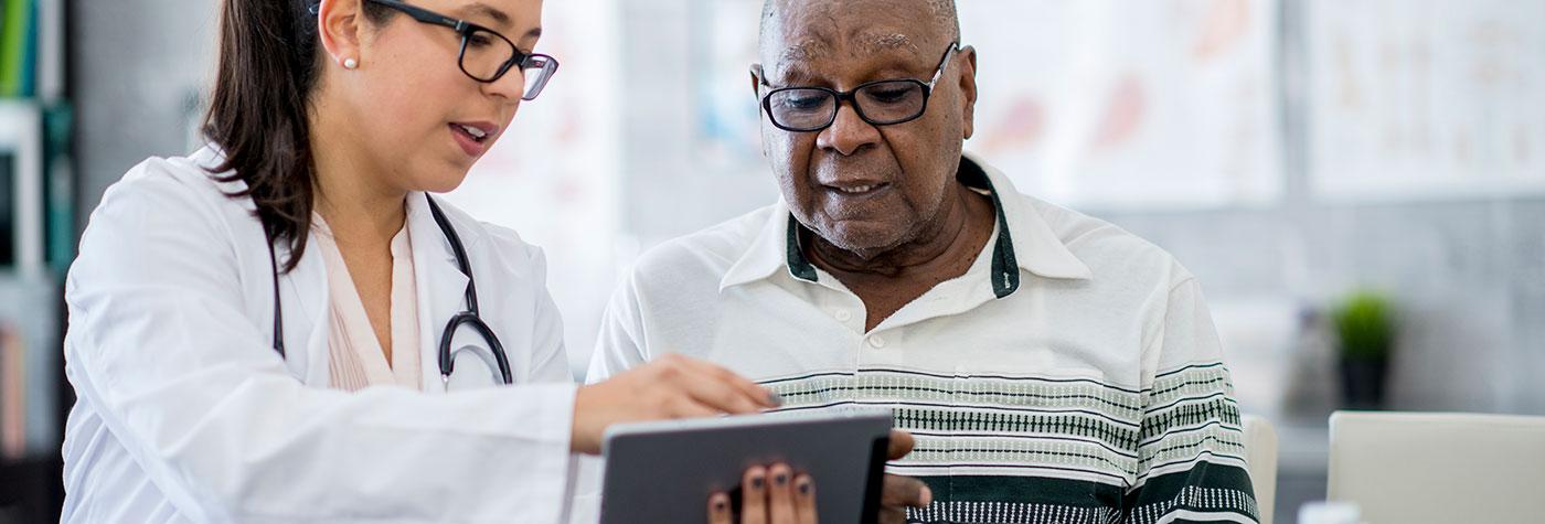 Female doctor uses a tablet to discuss test results with an older Black male patient.