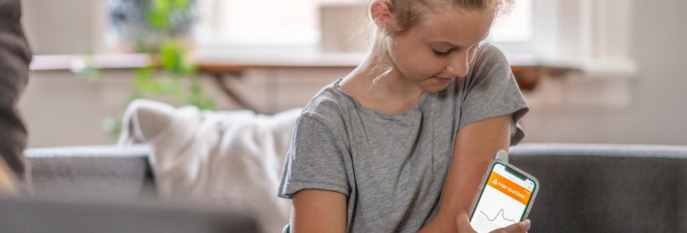 A preteen girl uses her smartphone to check a high blood glucose reading transmitted by her continuous glucose monitor.