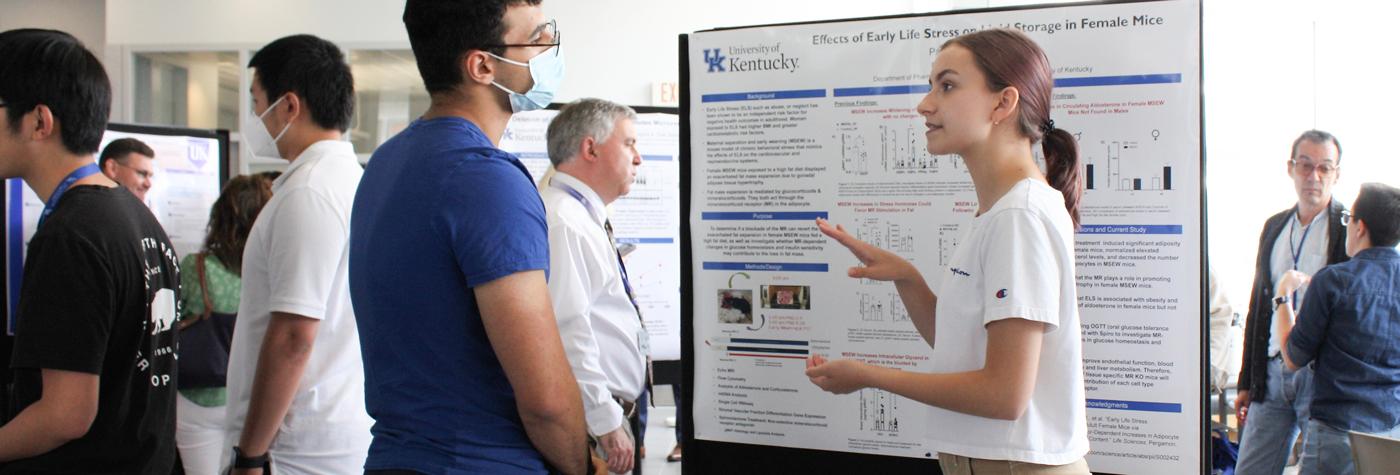 A student researcher discusses their poster with a research symposium attendee. 