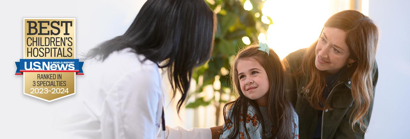 A UK HealthCare provider wearing her white coat speaks to a mother and her young daughter. A badge on the photo reads: "US News & World Report Best Children's Hospitals, Ranked in 3 Specialties, 2023–2024.