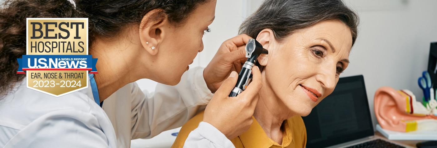 A provider uses an otoscope to look in a patient's ear. Superimposed on the image is a badge that reads U.S. News and World Report Best Hospitals - Ear, Nose & Throat - 2023–2024