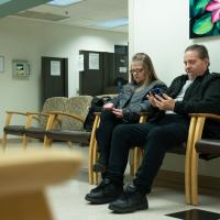 Deborah and Ron, both seated, scroll their phones while waiting for an appointment at UK HealthCare.