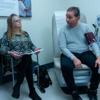 Deborah and Ron, both seated in a patient room. Ron is having his blood pressure taken.