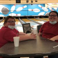 A photo of Abby and Drew smiling while sitting at a table in front of the lanes at a bowling alley.