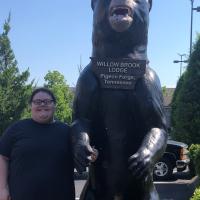 A photo of Abby smiling while posing with a large bear statue at the Willow Brook Lodge in Pigeon Forge, TN.