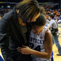 A close-up photo of Amber, dressed in her game uniform, side hugging one of her coaches as they appear to talk on the sidelines of the court.