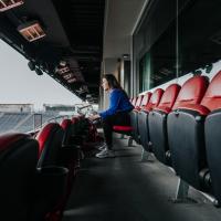 Arin sits in a red seat at the soccer stadium and stares down at the field.