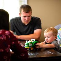 Caleb and Amelia watch Cason play with a toy tractor at their dining room table.