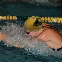 A photo of Callie swimming. She is wearing a dark suit, googles, and a yellow UNCW swim cap.