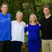 Coach O’Connor and her family gather around to take a picture outside. Beside her is her brother, Trent Martin, a white male in a black shirt; her mother, Donna Martin, an older white woman with blonde hair, wearing a white blouse; and her father, an older white man wearing a blue UK shirt.
