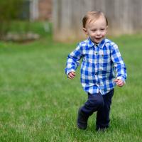 Michael runs across an open field. He is wearing a blue and white checkered shirt with navy blue pants.