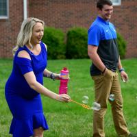 Coach O’Connor smiles as she makes bubbles in the air with her husband. He is a white man with brown hair, wearing a black and blue shirt.