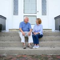 E and Cary sit on the front steps of their home, looking at each other and smiling.