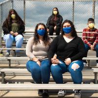 Faith and her mom wear blue face masks and hold hands, while her three siblings wear masks sitting behind them.