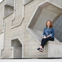 Fielden smiles at the camera as she sits on a giant sculpture of the UK logo outside the student center.