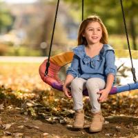 A photo of Kailey sitting on a colorful, circular swing as she looks off into the distance.