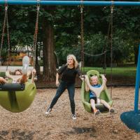 Kelley pushes Gabriella and Olivia on a green swing set at the park.