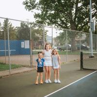 The Buffano sisters stand next to each other on a tennis court. Isabella, the oldest, has her arms around her younger sisters. All are smiling.