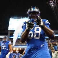 With an arena full of fans behind him, Kenneth stands on the football field and smiles as he points at the camera. He is wearing his blue UK uniform with number 68 on his chest.