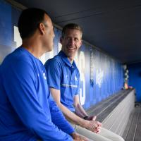 A candid photo of Matt and Nick smiling and talking on the bench in the dugout.