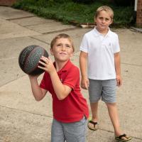 Max and his twin brother play basketball. Max is holding the ball and squinting up at the net, ready to shoot.