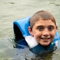 A portrait of Max, wearing a life jacket, floating in the lake. His hair is wet and he’s smiling.