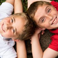 An overhead close-up shot of Max and his twin brother. Both are laying on the ground and have their hands behind their heads. Both are smiling.