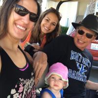 A selfie of Gary with his daughters Tracy and Maria, and his granddaughter Marley while riding in a golf cart. Murphie is a white female toddler with brown eyes, and is wearing a pink and green bucket hat.
